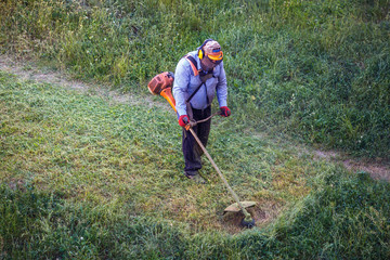 Top view fat dirty lawnmover man worker cutting dry grass with lawn mower.