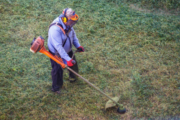 Top view fat dirty lawnmover man worker cutting dry grass with lawn mower.