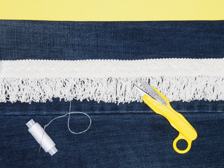 Lace, thread, scissors on jeans and yellow background. Sewing still life