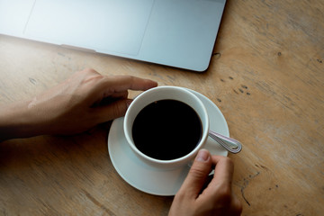 A cup of coffee on desk, Cup of coffee in hand, Men hand hold mug of black coffee, Close up concept.