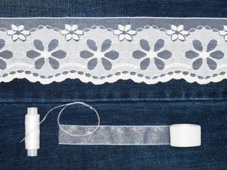 White lace, threads with needle, ribbon on a jeans background. Sewing still life