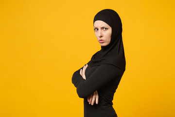 Sad upset crying confused young arabian muslim woman in hijab black clothes posing isolated on yellow wall background, studio portrait. People religious Islam lifestyle concept. Mock up copy space.