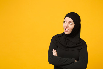 Sad upset crying confused young arabian muslim woman in hijab black clothes posing isolated on yellow wall background, studio portrait. People religious Islam lifestyle concept. Mock up copy space.