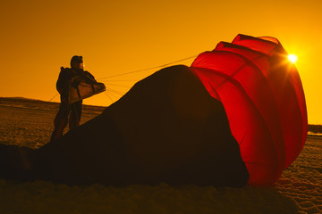 Silhouette of the skydiver next to the partially filled canopy of the parachute after landing on the field, a snapshot in warm tones. Orange filter. Parachute jumps.