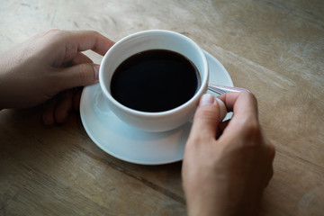 A cup of coffee on desk, Cup of coffee in hand, Men hand hold mug of black coffee, Close up concept.