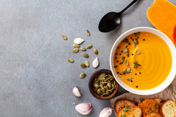 Healthy and delicious autumn pumpkin cream soup in bowl served with seeds and crouton on stone table top view.