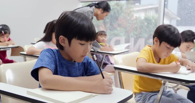 Little boy writing to book at classroom. Teacher take care to her student for lesson. Education concept.