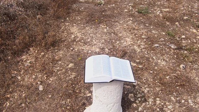 Bible laying open on a pillar, the wind is turning over the pages in slow motion.