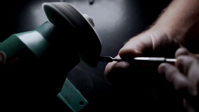 Close-up, worker sharpens manicure tools on grindstone, sparkles in slow-motion