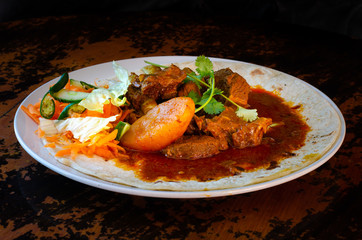 A mutton curry roti with sambals - an iconic Durban meal consisting of a roti topped with mutton curry and gravy. The sambals are grated carrot with chopped chilli.