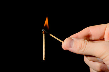 A hand with a lit match sets fire to a new match on a black background.