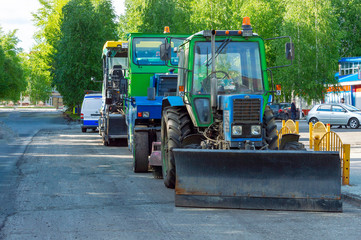 Standing on a city street in a row road repair machines.  Tractor, asphalt tamping roller and asphalt paver.   