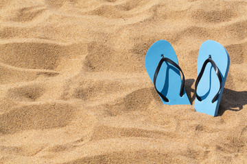 Fototapeta na wymiar Summer background of beach and shoes on sand. Blue flip flops on the sunny tropical beach.