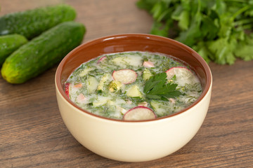Summer yogurt cold soup with radish, cucumber, and dill on wooden table. Russian cold vegetable soup on yogurt. Okroshka. 