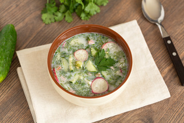 Summer yogurt cold soup with radish, cucumber, and dill on wooden table. Russian cold vegetable soup on yogurt. Okroshka. 