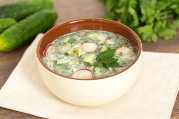 Summer yogurt cold soup with radish, cucumber, and dill on wooden table. Russian cold vegetable soup on yogurt. Okroshka. 