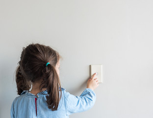 Rear view of little girl turning off Australian light switch on neutral wall background with copy...