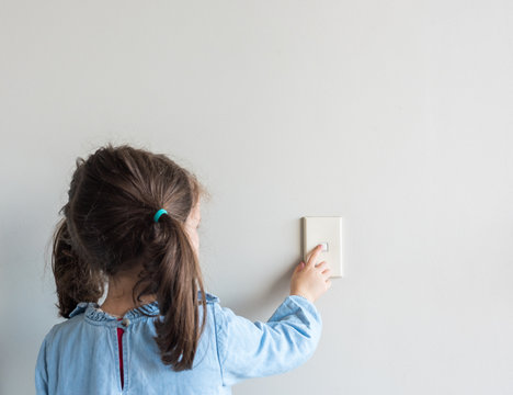 Rear view of little girl turning off Australian light switch on neutral wall background with copy space (selective focus)