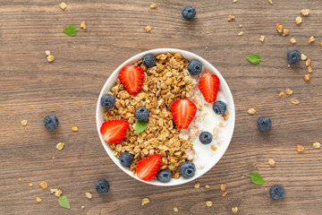 Healthy smoothie bowl with granola, yogurt, strawberry and fresh blueberries on wooden background. Breakfast smoothie bowl, top view.