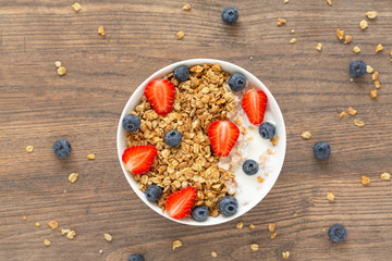 Breakfast smoothie bowl. Healthy smoothie bowl with granola, yogurt, strawberry and fresh blueberries on wooden background. Top view.