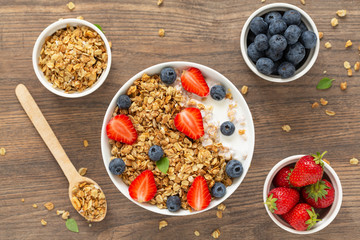 Healthy smoothie bowl with granola, yogurt, strawberry and fresh blueberries on wooden background. Breakfast smoothie bowl, top view.