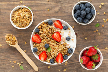 Healthy smoothie bowl with granola, yogurt, strawberry and fresh blueberries on wooden background. Breakfast smoothie bowl, top view.