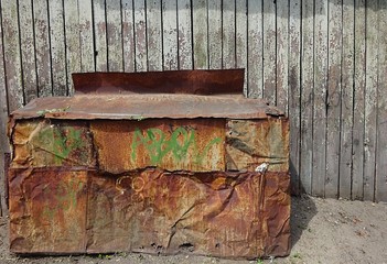 Old steel metal rust rustic storage box case in the yard and vintage aged wood wooden fence with cracked texture weathered surface crackle paint effect 
