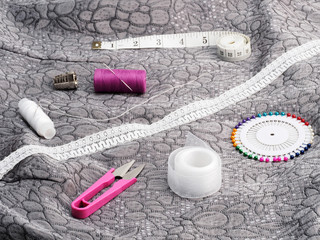 Tailor's tools – white lace, threads, scissors, ribbon, pins, thimble, tape measure on a background of gray fabric. Stitching still life