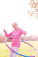 Active senior woman hula hooping in park © MDBPIXS