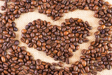 Coffee beans on a background of burlap. The grains are laid out in the shape of a heart. Place for text. Concept of making coffee, coffees.