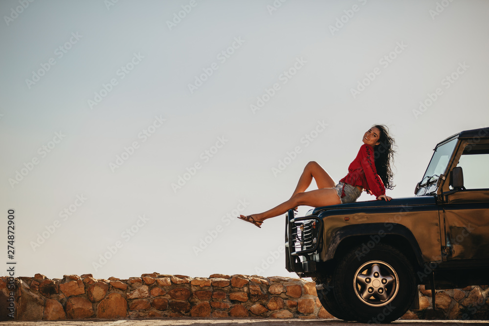 Wall mural Beautiful woman sitting on car hood