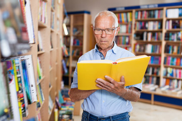 Focused elderly man looking for information in books in bookstore