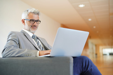 Cheerful businessman looking at laptop in lounge area
