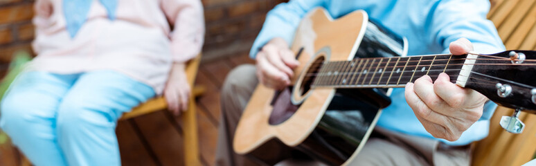 panoramic shot of senior man playing acoustic guitar near wife