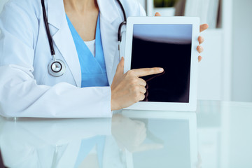 Female doctor using tablet computer while sitting at the workplace, close-up of hands. Medicine, healthcare and help concept