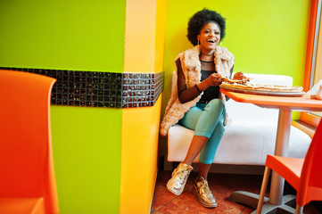 African woman with pizza sitting at bright colored restaurant.