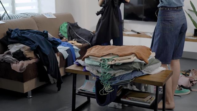two women are laying clothes in room of home together, sorting wardrobe, selecting good and bad gowns