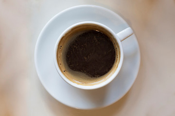 Cup of black coffee on white plate on beige table. Top view, flat lay, copy space, mock up