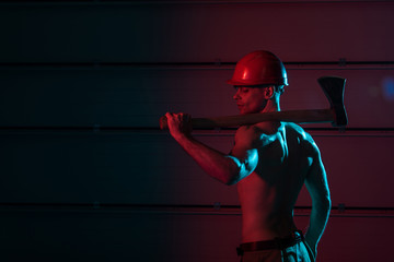 Fototapeta na wymiar Sexy shirtless fireman in protective helmet holding flat head axe in darkness