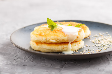 Cheese pancakes on a blue ceramic plate with milk sauce on a gray concrete background.