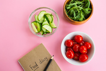 Diet concept. Vegetables and food diary on a pink background. Top view