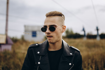 Young sexy man in leather jacket and sunglasses standing outdoor