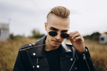 Young sexy man in leather jacket and sunglasses standing outdoor