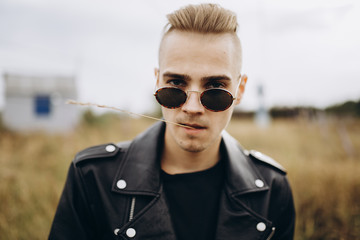 Young sexy man in leather jacket and sunglasses standing outdoor