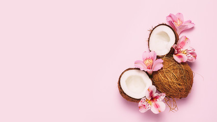 Broken coconut with tropic flowers on pink background.