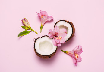 Obraz na płótnie Canvas Broken coconut with tropic flowers on pink background.