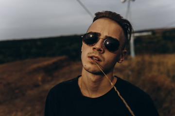 Young sexy man in black shirt and sunglasses standing outdoor. Dark key photo