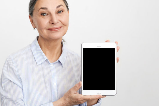 E-commerce, wifi, electronic devices and age concept. Studio image of happy elegant gray haired mature woman using high speed internet connection on digital tablet, showing blank copyspace display - Powered by Adobe