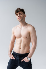 pensive shirtless man with hands in pockets isolated on grey