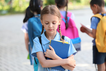 Sad little girl and her classmates outdoors